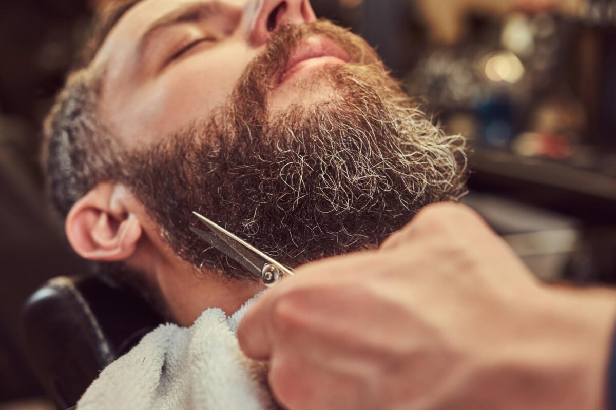 professional hairdresser explaining how often should you trim your beard and modeling beard with scissors comb barbershop close up photo