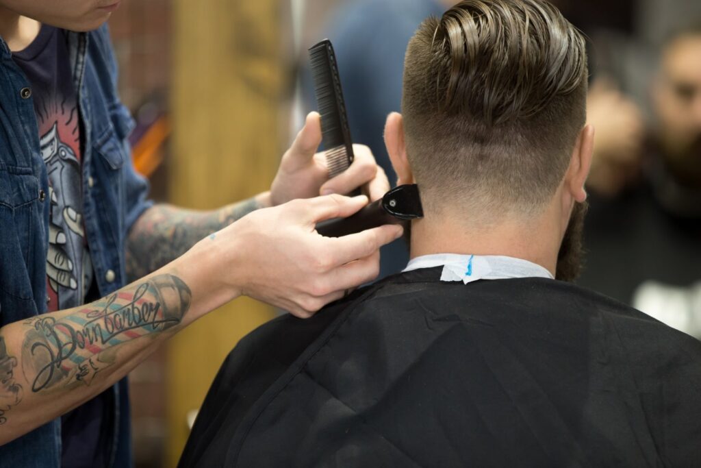 The back of a man head receiving a fix for his bad haircut with a hair clipper