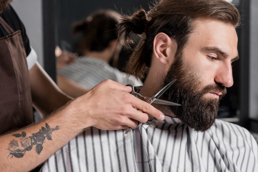 close up hairdresser cutting male customer beard